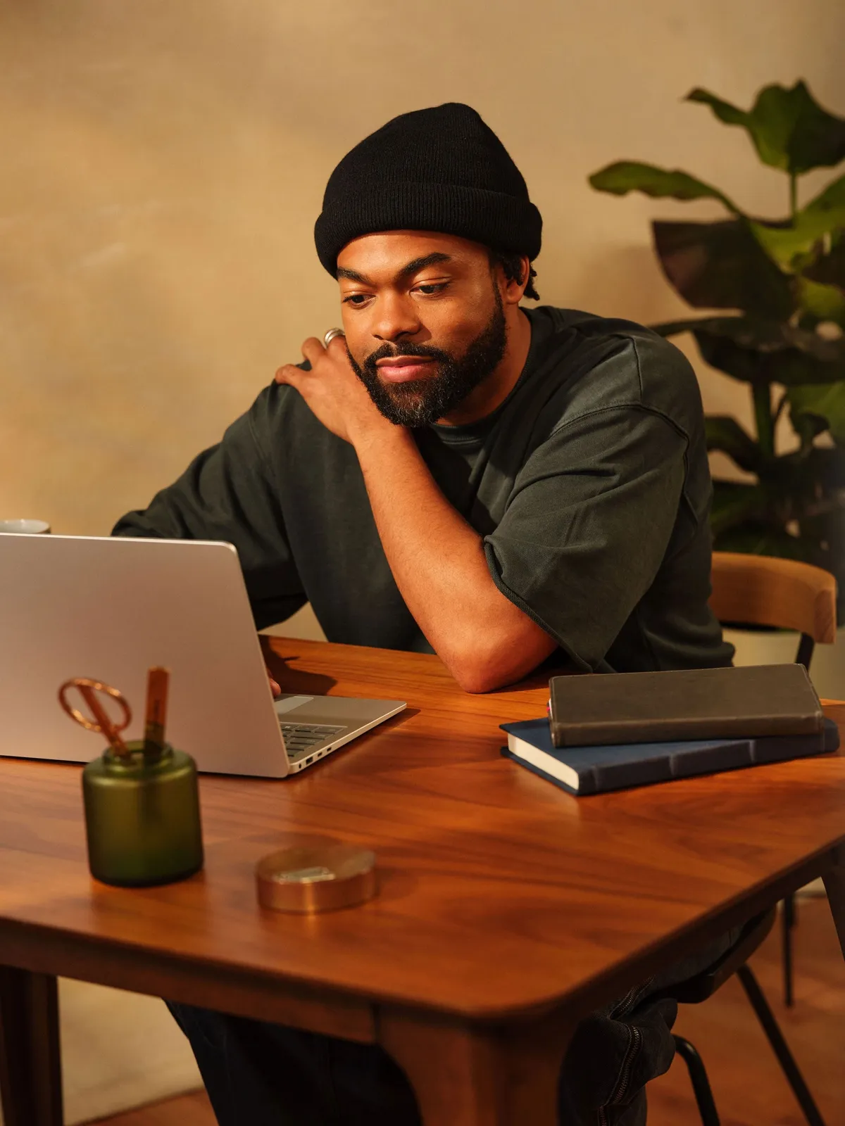 A vendor in a beanie working on a laptop at a wooden desk